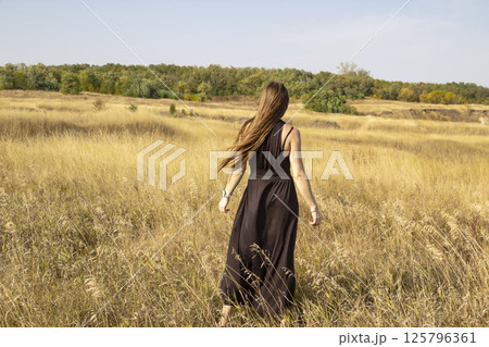 Pretty young dark haired woman in black dress stand in field. Beautiful girl outdoor in the field enjoy with freedom Pretty young dark haired woman in black dress stand in field. Beautiful girl outdoor in the field enjoy with freedom 125796361