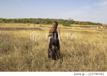 Pretty young dark haired woman in black dress stand in field. Beautiful girl outdoor in the field enjoy with freedom Pretty young dark haired woman in black dress stand in field. Beautiful girl outdoor in the field enjoy with freedom 125796362