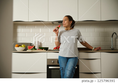 Woman Enjoying Fresh Fruit in a Modern Kitchen Setting Woman Enjoying Fresh Fruit in a Modern Kitchen Setting 125796391