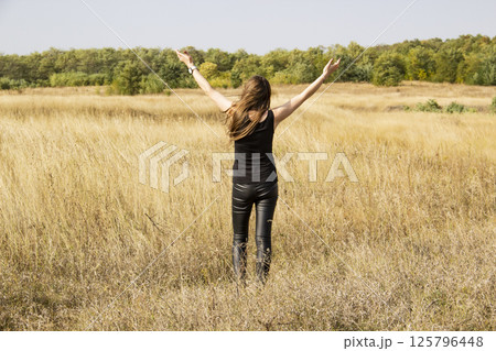 Beautiful young dark haired woman in black clothes stand in field. Pretty girl stand outdoor in the field and looking up with hands up. Beautiful young dark haired woman in black clothes stand in field. Pretty girl stand outdoor in the field and looking up with hands up. 125796448