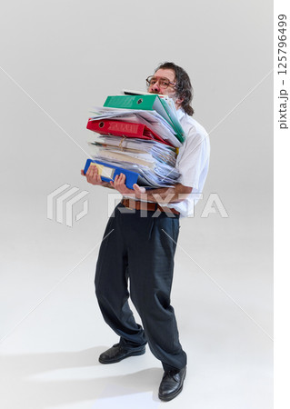 Office worker holding huge stack of binders and documents, being completely buried and overwhelmed by endless paperwork. Office worker holding huge stack of binders and documents, being completely buried and overwhelmed by endless paperwork. 125796499