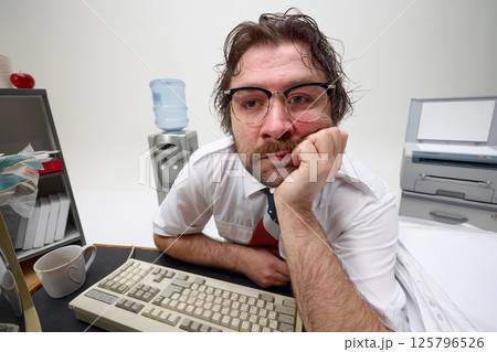 Frustrated office worker leans on desk, looks tired, surrounded by retro tech and paperwork, showing burnout and lack of motivation Frustrated office worker leans on desk, looks tired, surrounded by retro tech and paperwork, showing burnout and lack of motivation 125796526