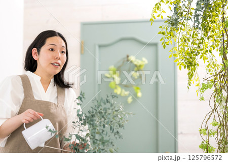 室内で植物の水やりをする笑顔の大人女性｜花屋園芸店教室イメージ｜ウェルビー女子｜ウェルビーイング 125796572