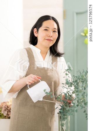 室内で植物の水やりをする笑顔の大人女性｜花屋園芸店教室イメージ｜ウェルビー女子｜ウェルビーイング 125796574