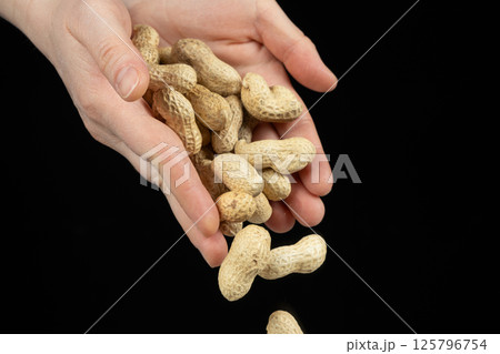 Hands pouring whole unpeeled peanuts, black background. 125796754
