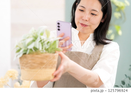 室内で植物を撮影するミドル女性|花屋園芸店教室イメージ|ウェルビー女子|ウェルビーイング 室内で植物を撮影するミドル女性|花屋園芸店教室イメージ|ウェルビー女子|ウェルビーイング 125796924