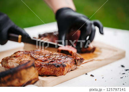 Chef slicing juicy grilled steak on wooden cutting board. Chef slicing juicy grilled steak on wooden cutting board. 125797141