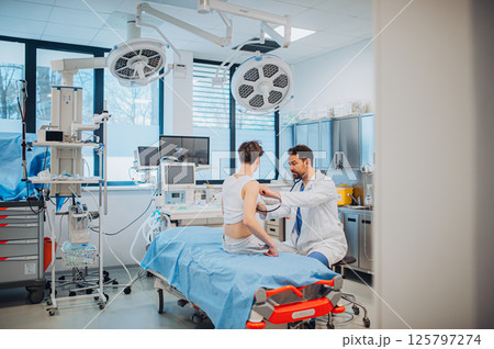 Teen boy undergoing medical checkup with doctor in hospital room. 125797274