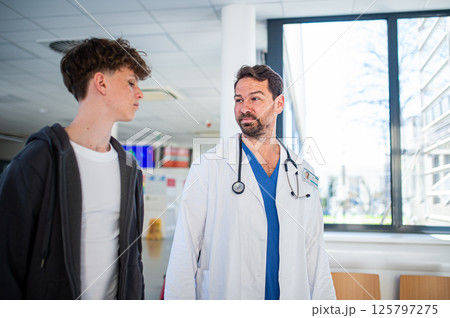 Doctor walking with teenage patient after successful medical procedure in hospital. 125797275