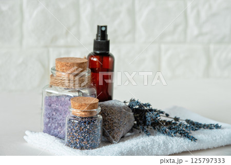Lavender Spa Set with Dried Flowers and Bath Salts. Relaxing Spa Arrangement. Lavender flowers, bath salts, dried buds in glass jars, spray bottle, and sachet on white towel 125797333