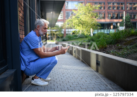 Healthcare worker outside hospital and checking phone during break. Healthcare worker outside hospital and checking phone during break. 125797334