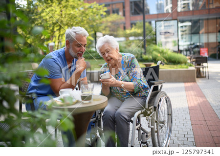 Male nurse having cup of coffee with senior patient in a wheelchair. 125797341