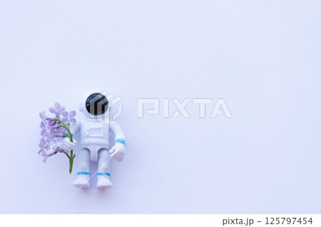 A toy spaceman holding lilac flowers. On a white background , copy space. 125797454