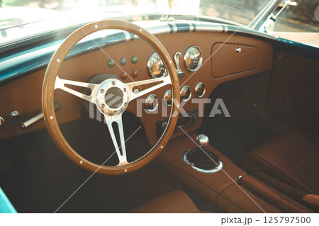 Vintage classic car interior featuring leather seats, chrome gauges, wooden steering wheel and polished dashboard Vintage classic car interior featuring leather seats, chrome gauges, wooden steering wheel and polished dashboard 125797500