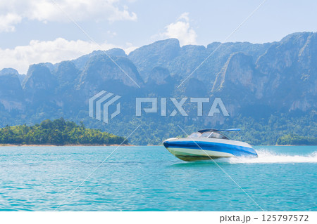 A speedboat gliding through the turquoise waters of Cheo Lan Lake against the backdrop of the mountains of Khao Sok Park on a sunny day in a tropical paradise in Thailand 125797572