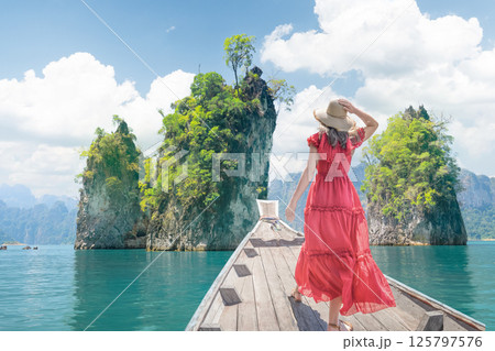 A Woman female solo traveler in a Red dress and hat on a Thai boat near the famous Three Rocks site on Cheo Lan Lake in Thailand. Travel and tours to the sea and islands of Thailand and Southeast Asia 125797576