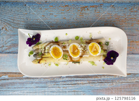 Baked asparagus with boiled egg in big white plate on blue background Baked asparagus with boiled egg in big white plate on blue background 125798116