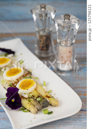 Baked asparagus with boiled egg in big white plate on blue background 125798121