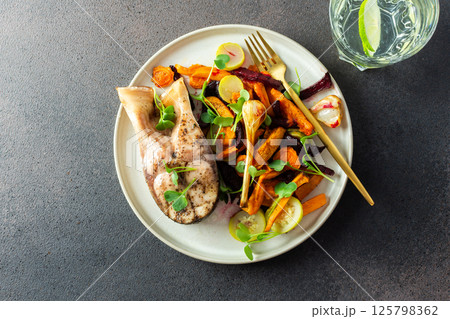 Baked silver carp with roasted carrots, zucchini, beets, and garlic , perfect for a healthy and delicious breakfast or lunch, plates with food on a dark background 125798362