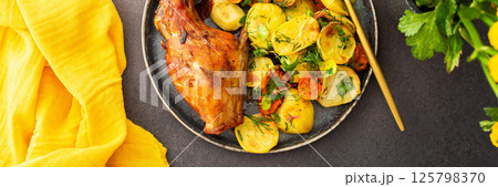 Baked rabbit with potatoes and carrots, a set table with food, a glass of wine and a vase of flowers 125798370