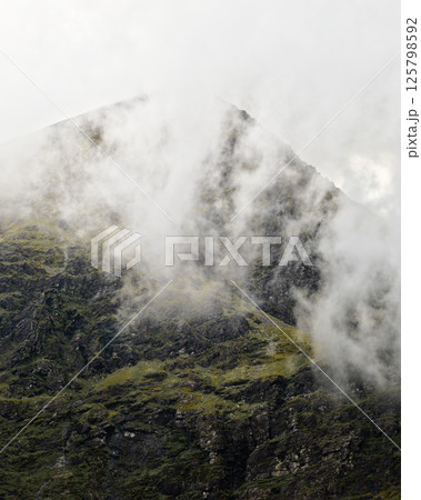 Misty landscape surrounding Carrauntoohil in Ireland showcases its stunning natural beauty during a cloudy day. 125798592