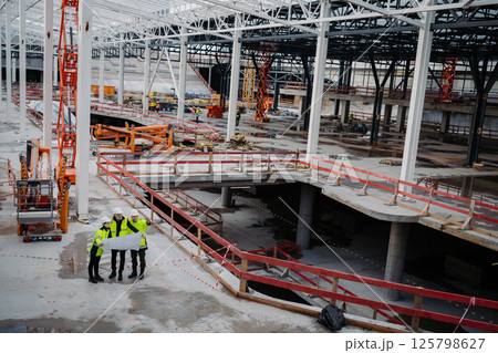 Team of engineers and construction workers reviewing blueprints, building site. Team of engineers and construction workers reviewing blueprints, building site. 125798627