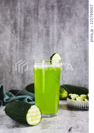 Fresh cucumber juice in a glass and cucumber pieces in a bowl on the table vertical view 125799007