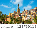 Saint Michel Archange basilica with tall yellow bell tower surrounded by old colorful buildings in Menton, France. 125799118