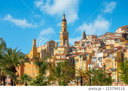 Saint Michel Archange basilica with tall yellow bell tower surrounded by old colorful buildings in Menton, France. 125799118