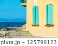 A yellow walled building with vibrant turquoise shutters overlooks the azure waters of Saint-Tropez. 125799123