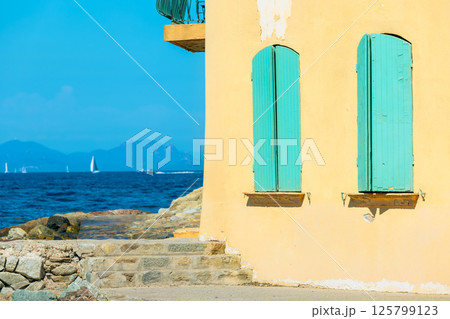 A yellow walled building with vibrant turquoise shutters overlooks the azure waters of Saint-Tropez. A yellow walled building with vibrant turquoise shutters overlooks the azure waters of Saint-Tropez. 125799123