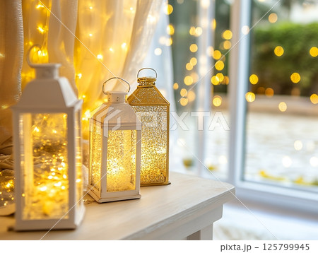 Three lanterns on a white table with fairy lights and a window in the soft background light 125799945
