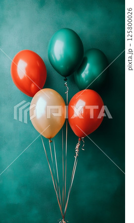 A group of colorful balloons floating against a teal wall with long curly ribbons attached to them 125800026