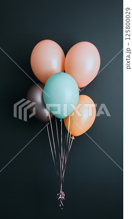 A bunch of colorful party balloons with silver ribbons against a dark gray colored background wall A bunch of colorful party balloons with silver ribbons against a dark gray colored background wall 125800029