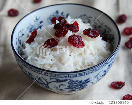 A bowl of white rice topped with dried cranberries sitting on a light colored tablecloth surface A bowl of white rice topped with dried cranberries sitting on a light colored tablecloth surface 125800140