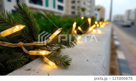 Bright yellow string lights hang over a lush garden filled with cypress trees, creating a warm atmosphere on a summer evening 125800678