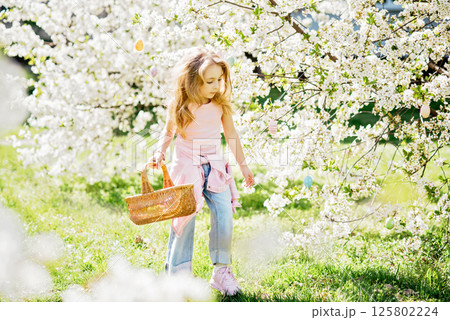 Easter egg hunt. Girl child Wearing Bunny Ears Running To Pick Up Egg In Garden. Easter tradition. Baby with basket full of colorful eggs. Easter egg hunt. Girl child Wearing Bunny Ears Running To Pick Up Egg In Garden. Easter tradition. Baby with basket full of colorful eggs. 125802224