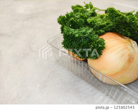 Fresh onion and parsley resting in plastic container on kitchen counter copy space preparing vegetables for making soup Fresh onion and parsley resting in plastic container on kitchen counter copy space preparing vegetables for making soup 125802543