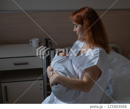 Caucasian woman holding newborn son while sitting on couch in maternity hospital ward. Caucasian woman holding newborn son while sitting on couch in maternity hospital ward. 125803088