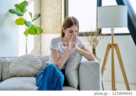 Sad teenage girl 17-18 years old sitting at home on the couch 125804042