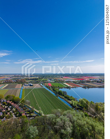 Aerial view of peaceful suburban neighborhood surrounded by fields and canals. Neat rows of houses with red roofs reflect in the water set against a backdrop of farmland and open skies. Beautiful lake Aerial view of peaceful suburban neighborhood surrounded by fields and canals. Neat rows of houses with red roofs reflect in the water set against a backdrop of farmland and open skies. Beautiful lake 125804067