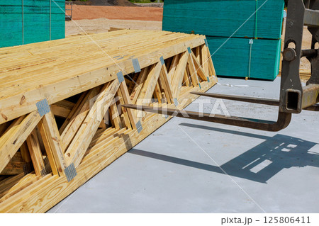 Workers maneuvering wooden trusses using forklift on construction site under works day 125806411