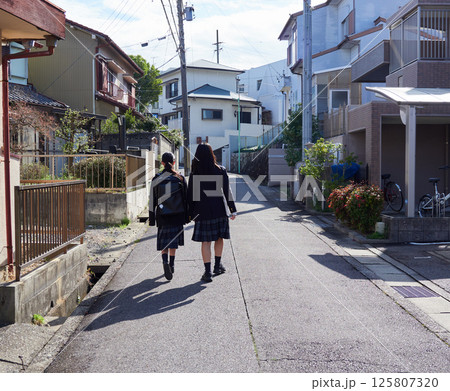 春の朝の住宅地に登校中の姉妹学生の後ろ姿 春の朝の住宅地に登校中の姉妹学生の後ろ姿 125807320