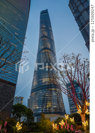 Twilight view of Shanghai Tower illuminated against dusk sky with glowing butterfly installations and floral decorations at its base Twilight view of Shanghai Tower illuminated against dusk sky with glowing butterfly installations and floral decorations at its base 125809247