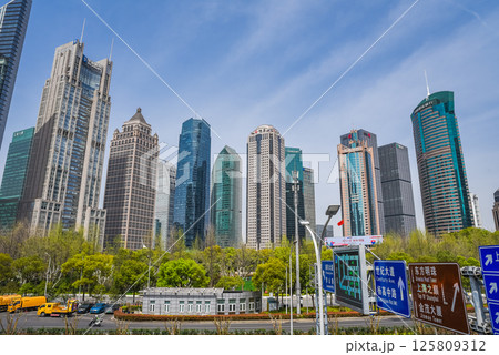 Shanghai, China - 1 April 2025: Modern Pudong district skyline showcasing diverse architectural styles - glass towers, classical and futuristic buildings, framed by spring foliage in foreground park. 125809312