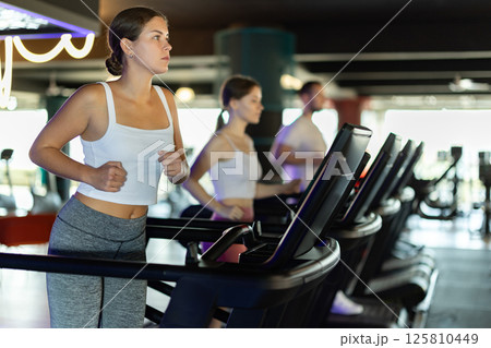 Girl in gym runs with help of treadmill 125810449
