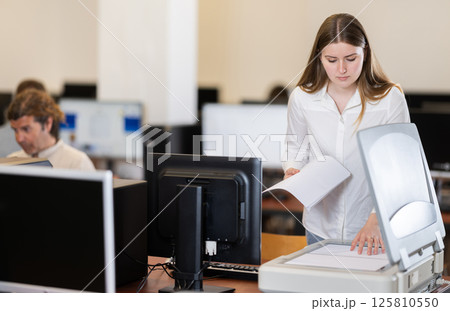 Girl puts paper document into copier, makes copy using office appliances 125810550