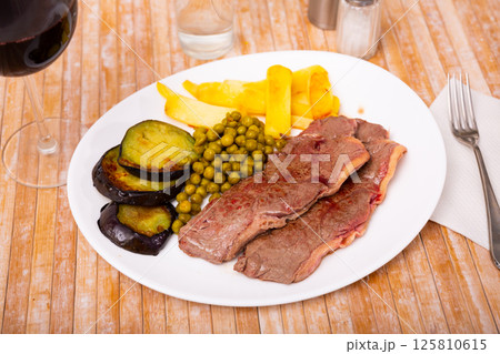 Baked beef steaks with fries, aubergine slices and peas Baked beef steaks with fries, aubergine slices and peas 125810615