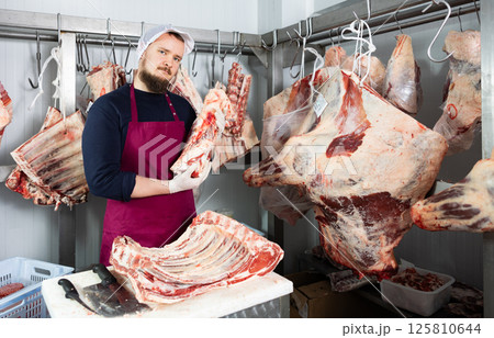 Male butcher shop butcher shows raw chopped carcasses and ribs 125810644