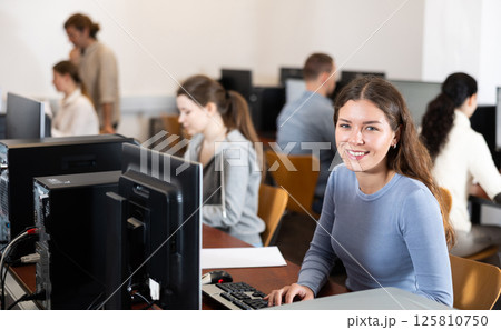 Young woman student of computer courses looks at monitor screen, types on keyboard and does work 125810750